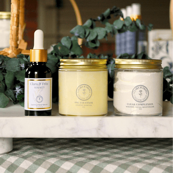 The Clear Complexion Routine skincare products including oil cleanser, calming serum, and facial moisturizer on a marble counter.