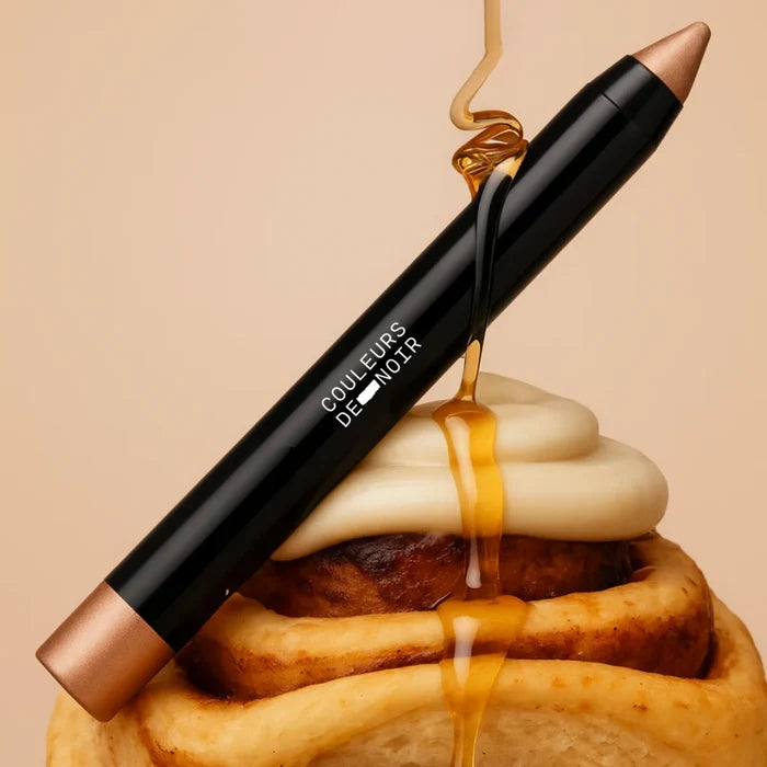 Black cosmetic pencil with gold accents on a waffle background, featuring the brand 'COULEURS DE NOIR'.