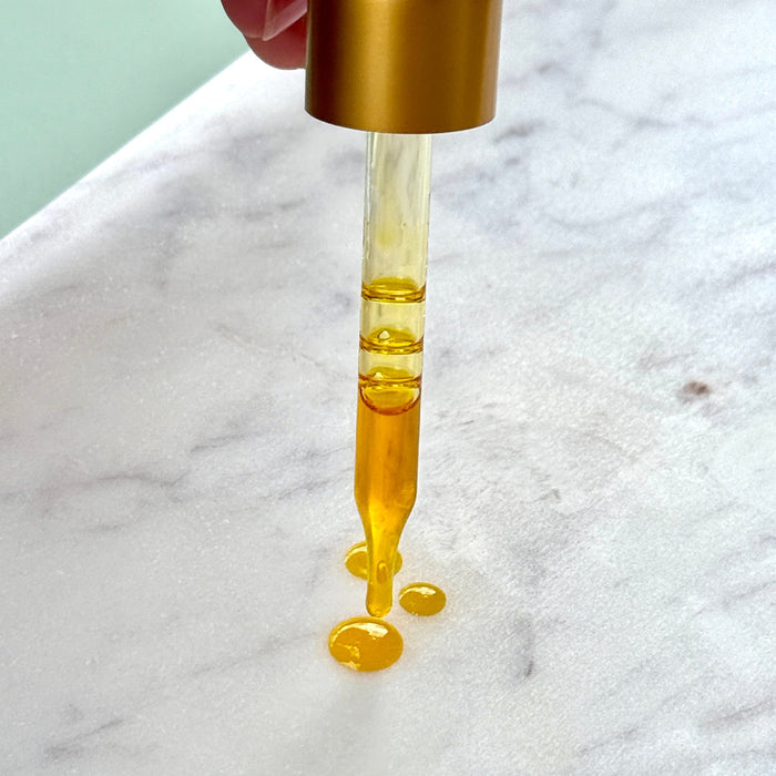 Radiance Instant Glow Facial Serum dropper with golden serum on marble surface, highlighting its hydrating and revitalizing properties.