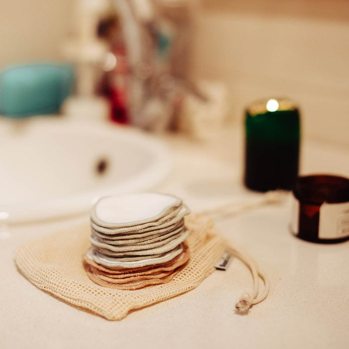 Stack of round reusable makeup remover pads resting on a beige mesh bag.